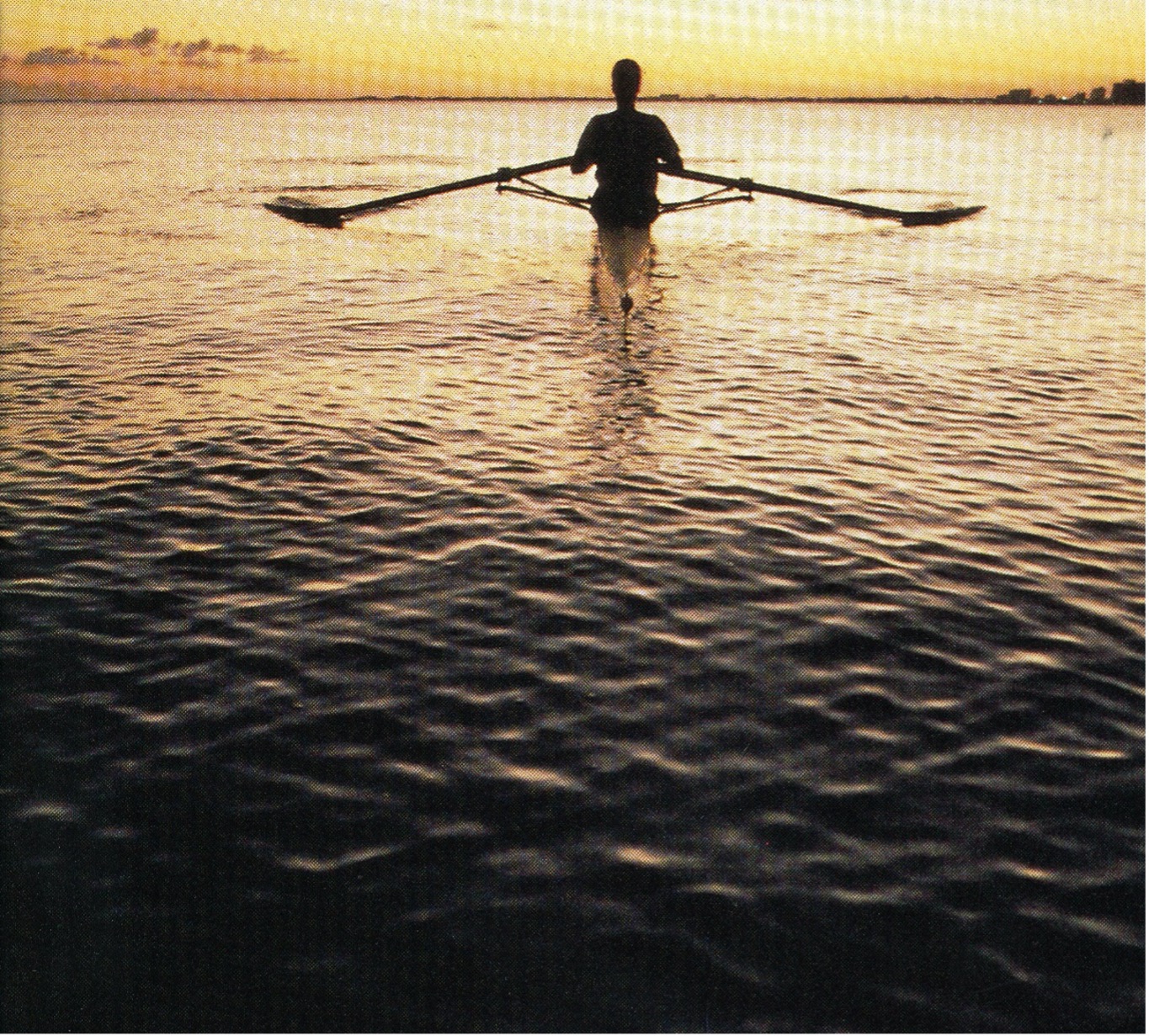 A solo rower silhouetted against a sunset on calm water.